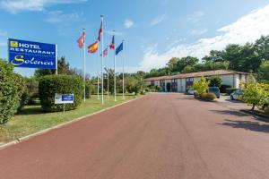 a road with flags in front of a hotel with a sign at Hôtel Solenca in Nogaro