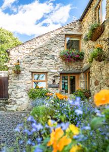 una casa de piedra con flores delante en The Wayside and Whisky Barn, en Whitbeck