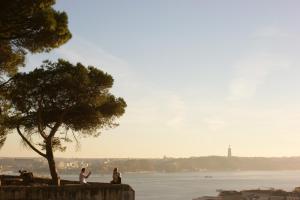 people sitting on a wall near the water with a tree at Casa em Alfama in Lisbon