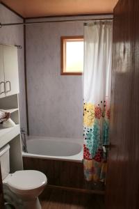 a bathroom with a tub and a toilet and a shower curtain at Cabañas Río Quemille in Huillinco
