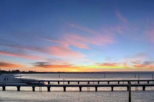 ein Pier am Strand mit Sonnenuntergang im Hintergrund in der Unterkunft The Sebel Busselton in Busselton