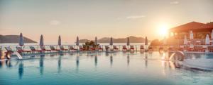a large swimming pool with chairs and the sun setting at Sun Gardens Dubrovnik in Dubrovnik