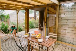 une femme assise sur une terrasse avec une table en bois dans l'établissement Naturéo, à Seignosse