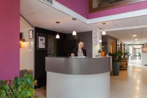 a man standing behind a counter in a lobby at The Originals City, Hôtel Castel Burgond, Dijon Ouest (Inter-Hotel) in Dijon