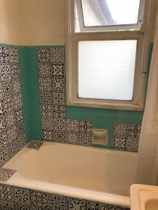 y baño con bañera, ventana y azulejos. en Casa Ryan, en Santiago