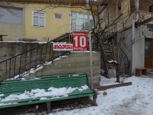 una panchina verde seduta di fronte a un edificio nella neve di Paata's Guesthouse a Borjomi