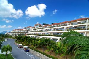 a large white building with palm trees and a street at Kanucha Bay Hotel & Villas in Nago