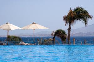 a swimming pool with two umbrellas and the ocean at Cleopatra Luxury Resort Sharm El Sheikh in Sharm El Sheikh