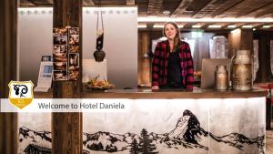 une femme debout derrière un comptoir avec une photo de montagne dans l'établissement Hotel Daniela, à Zermatt
