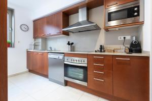 cocina con armarios de madera, fogones y microondas en Apartamento Camp Nou 101, en Hospitalet de Llobregat