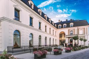 un grand bâtiment blanc avec des bancs dans une cour dans l'établissement Hotel Mansor, à Ząbki