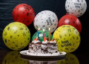 einen Geburtstagskuchen mit Kerzen vor Ballons in der Unterkunft Alba Hotel Meru in Meru