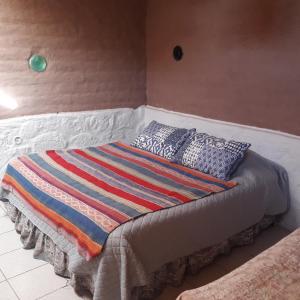 Una cama con una manta colorida y almohadas. en Casa Buenavista, en San Pedro de Atacama