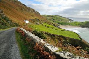 Muckross School House في Kilcar: منزل صغير على تلة بجوار طريق