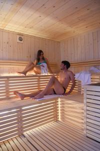 a man and a woman sitting in a sauna at Residence & Wellness 3MILA in Peio Fonti