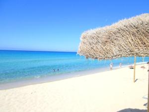 a straw umbrella on a beach with people in the water at Sardinia Yellow House in Solanas