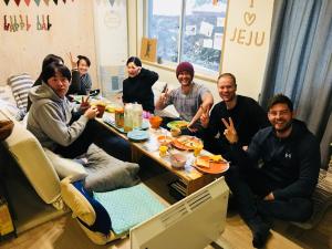 un grupo de personas sentadas alrededor de una mesa comiendo comida en Greenday Guesthouse en Jeju
