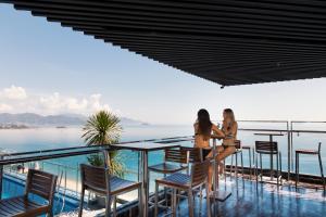 two women sitting at a table on a balcony overlooking the ocean at Holi Beach Hotel & Apartments in Nha Trang