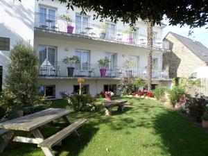 a garden with two picnic tables in front of a building at Hôtel du Littoral in Camoël