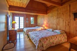 two beds in a room with wooden walls and wooden floors at Le Cent in Saguenay