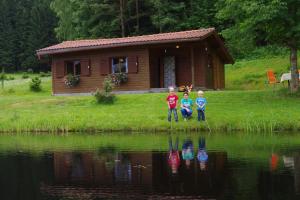 three children standing in front of a cabin next to a lake at Ferienhaus Forellenwirt in Grünbach