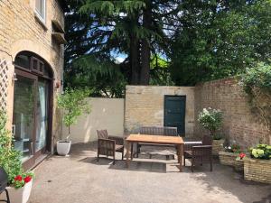 eine Terrasse mit einem Holztisch und Stühlen neben einer Ziegelwand in der Unterkunft The Coach House in Stamford