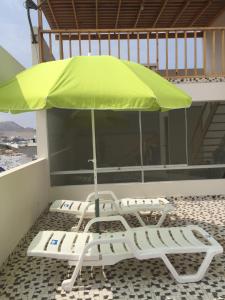 zielony parasol i 2 krzesła na balkonie w obiekcie Departamentos Playa San Bartolo w mieście San Bartolo