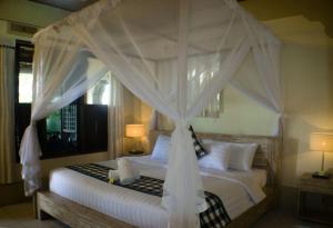 ein Schlafzimmer mit einem Himmelbett mit weißer Bettwäsche und Kissen in der Unterkunft Rumah Roda in Ubud + 37 Fotos