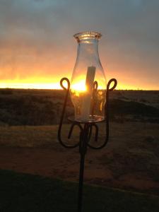 una vela en un jarrón de cristal con la puesta de sol en el fondo en Kamelruhe Guest House & Camping en Gochas