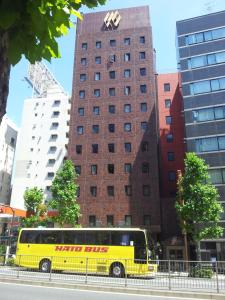 un autobús amarillo estacionado frente a un edificio alto en Ginza Capital Hotel Akane, en Tokio