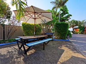 a picnic table with an umbrella and a bench at Riviera Motel Bundaberg in Bundaberg