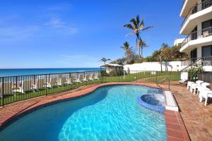 a swimming pool with chairs and the ocean in the background at Spindrift on the Beach - Absolute Beachfront in Gold Coast