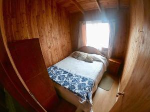 Cama pequeña en habitación de madera con ventana en Hostal Maitahue en Pucón