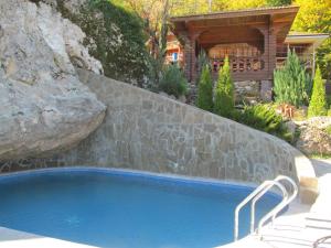 a swimming pool with a rock and a house at Guesthouse Lyubava in Kamennomostskiy