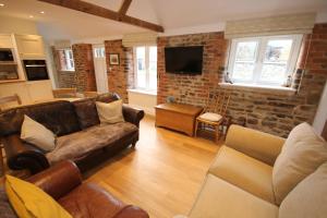 a living room with leather furniture and a brick wall at Bolton's Cottage in Oakham