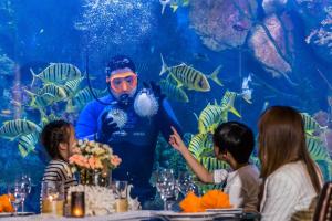 Amaranta Hotel - SHA Plus في بانكوك: رجل يقف أمام حوض سمك مع الأطفال