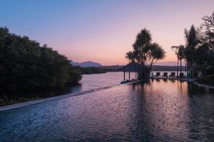 a pool of water with palm trees and a sunset at Mimpi Resort Menjangan in Banyuwedang
