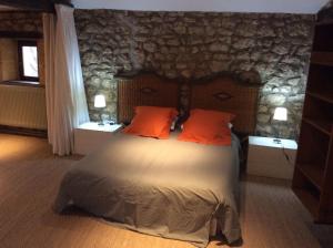 a bedroom with a bed with orange pillows and a stone wall at annexe du Mesnil in Le Tourne