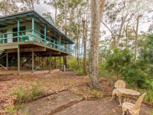 une maison dans les bois avec une table et des chaises dans l'établissement Fyshwicks Cottage, à Smiths Lake