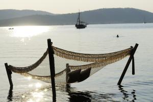 a hammock in the water with a boat in the water at Ekies All Senses Resort, a Member of Design Hotels in Vourvourou