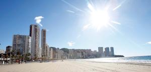 a beach with buildings and the sun in the sky at Hotel Lido in Benidorm