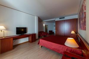 um quarto de hotel com uma cama vermelha e uma televisão de ecrã plano em Hotel Torre Normanna em Altavilla Milicia
