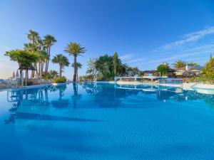 a large swimming pool with blue water and palm trees at Hotel Jardín Tecina in Playa de Santiago