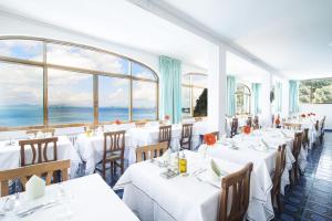 un ristorante con tavoli e sedie bianchi e finestre di Hotel Bagnitiello a Ischia