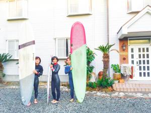 three women are holding surfboards in front of a house at Beach Side Inn Shirahama in Shimoda