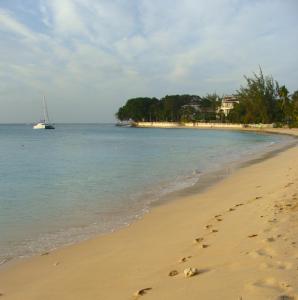 a beach with footprints in the sand and a boat in the water at Coral Lane Beach Apartments in Saint James