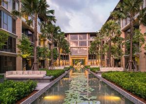 an exterior view of a building with a pond and palm trees at Baan mai khao apartment in Mai Khao Beach