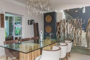 a dining room with a glass table and chairs at 11 on Fairway Beach Villa in Southbroom