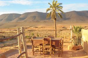 einen Tisch und Stühle in der Wüste mit einer Palme in der Unterkunft Tarmguist in Aït Boukha