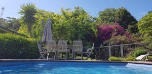 Un grupo de sillas y una sombrilla junto a una piscina. en Deloraine Stone Cottage, en Whangarei